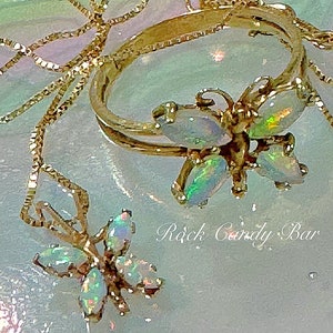 May include: Two gold necklaces with opal butterfly pendants. The necklaces are on a light blue background with the text "Rock Candy Bar".
