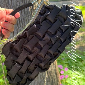 May include: Black satin clutch with a woven design. The purse has a silver-tone metal frame and a black handle. A silver chain strap is also attached. The text "Rock Candy Bow" is visible in the upper right corner.