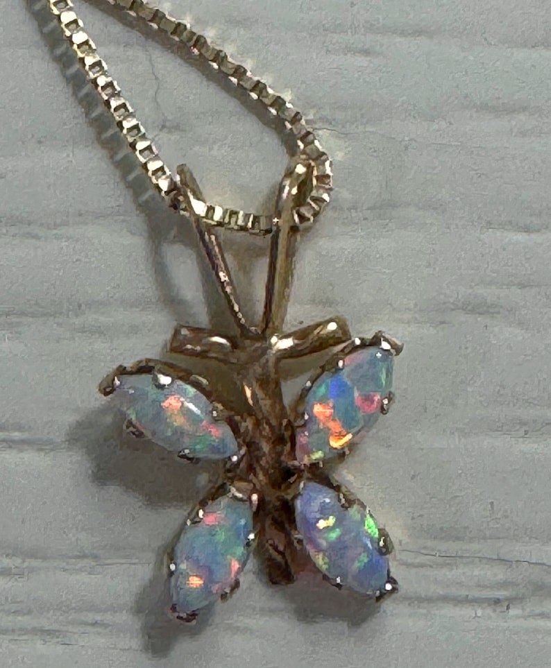 May include: A gold butterfly pendant necklace with five iridescent opal stones. The necklace has a delicate chain.