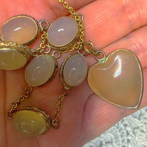 May include: A gold chain necklace with a heart-shaped pendant and several oval-shaped stones. The stones are a pale, translucent pink.