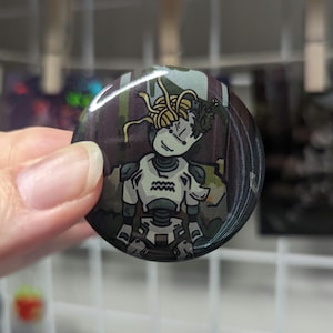 May include: Round button with a cartoon robot design. The robot has a white body with gray accents and a head of spaghetti and leaves. The background is a dark forest scene. The robot has the Aquarius symbol on its chest.