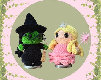 Könnte beinhalten: Ein 2-in-1-Bundle aus gehäkelten Witch Buddies. Einer ist eine grüne Hexe mit schwarzem Hut und Brille, die einen Besen hält. Der andere ist eine Prinzessin mit rosa Kleid, blonden Haaren und einer Krone. Der Hintergrund ist hellgrün und rosa.