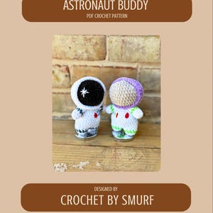以下が含まれることがあります： 黒いヘルメットと白い星、紫とベージュのヘルメットをかぶった2体の編みぐるみ宇宙飛行士。 赤と緑のアクセントが付いた白いスーツを着ています。 テキストには「ASTRONAUT BUDDY PDF CROCHET PATTERN」と「DESIGNED BY CROCHET BY SMURF」と書かれています。
