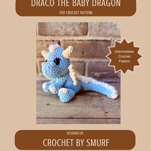 May include: A crocheted baby dragon in shades of blue and white, with large blue eyes and small horns. The image includes text that reads "DRACO THE BABY DRAGON" and "PDF CROCHET PATTERN". The design is by "CROCHET BY SMURF" and is an "Intermediate Crochet Pattern".