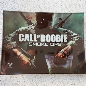 May include: Rectangular tray with the text "CALL OF DOOBIE SMOKE OPS" in white. The image features a person in military attire, holding a lighter and a bag of green herbs. The Syndicate logo is visible.