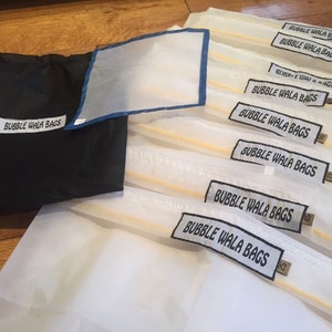 Könnte beinhalten: Ein Satz von zehn weißen Netz-Obst- und Gemüsesäcken mit schwarzen Etiketten, auf denen "BUBBLE WALA BAGS" steht. Die Säcke sind gefaltet und übereinander gestapelt. Im Hintergrund befindet sich eine schwarze Kordeltasche.