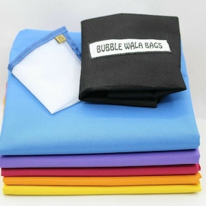 May include: A collection of brightly coloured fabric squares in shades of blue, purple, red, orange, and yellow. A white square with a blue trim and a black bag with the text "BUBBLE WALA BAGS" are on top. The fabric has a tight weave.