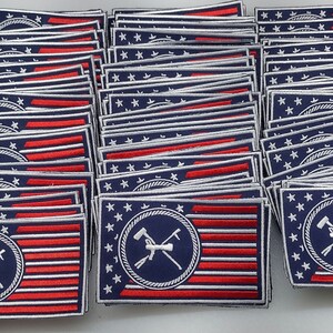 May include: A stack of blue and red embroidered patches with a white star pattern. Each patch features a white circle with a navy blue background and a crossed hammer and pickaxe design. The patches are arranged in a vertical stack.