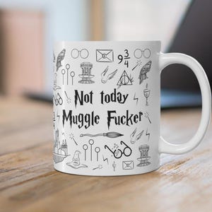 May include: White ceramic mug with black line art illustrations of various objects and the text "Not today Muggle Fucker". The mug has a white handle and is sitting on a wooden surface.