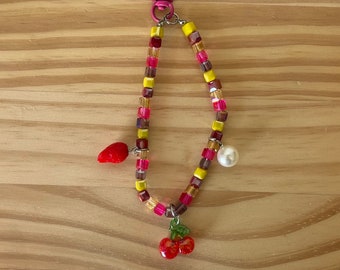 May include: A colorful beaded keychain with a pink metal clasp, a red strawberry charm, a white pearl charm, and a red cherry charm.