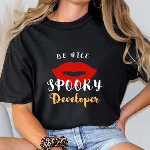 May include: Black t-shirt with a red vampire mouth graphic and the text "Be Nice Spooky Developer" in white and orange.