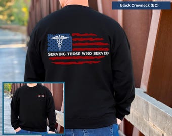 May include: Black crew neck sweatshirt with an American flag design. The flag features a blue field with a medical symbol and red and white stripes. The text "SERVING THOSE WHO SERVED" is printed below the flag.