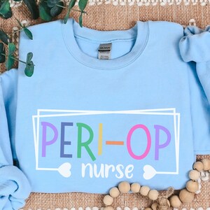 May include: Light blue sweatshirt with the text "PERI-OP nurse" in rainbow colors inside a white frame.