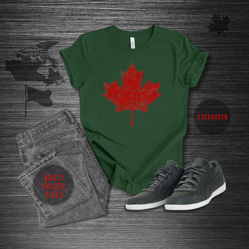 K&ouml;nnte beinhalten: Gr&uuml;nes T-Shirt mit einem roten Ahornblatt-Design im Used-Look. Dazu graue Jeans und dunkelgraue Sneaker mit wei&szlig;en Sohlen. Der Text "EVERGREEN" ist zu sehen.