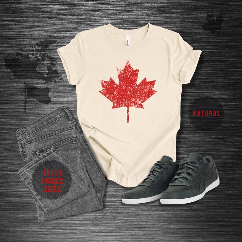 K&ouml;nnte beinhalten: Cremefarbenes T-Shirt mit einem roten Ahornblatt-Grafik-Design, kombiniert mit grauen Jeans und dunkelgrauen Turnschuhen. Das Shirt ist mit "NATURAL" und "ADULT UNISEX SIZES" beschriftet.