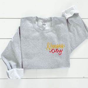 Puede incluir: Sudadera gris con un dise&ntilde;o bordado en amarillo y rojo que dice "Kansas City".