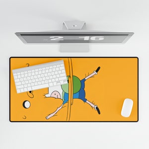 May include: A yellow desk mat with a cartoon illustration of a character from the animated series Adventure Time. The character is Finn the Human, and he is shown upside down, with his legs sticking out of a yellow wall. The desk mat also features a white keyboard and a white mouse.