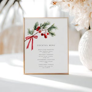 May include: A framed cocktail menu with a gold border. The menu features a watercolor illustration of a sprig of holly with red berries and a red ribbon. The menu lists four cocktails: Mistletoe Martini, Holiday Sangria, Cranberry Cocktail, and Christmas Punch.