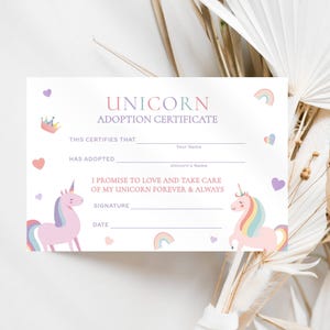 May include: A white unicorn adoption certificate with the words "UNICORN ADOPTION CERTIFICATE" in pink and purple. The certificate includes spaces to fill in the adopter's name, the unicorn's name, and a signature line. Two unicorns and rainbows decorate the certificate.