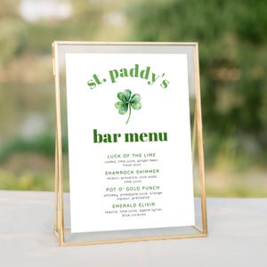 Może przedstawiać: Biały znak w złotej ramie, przedstawiający zieloną koniczynę i tekst "st. paddy's bar menu". Znak zawiera listę czterech opcji napojów: "Luck of the Lime", "Shamrock Shimmer", "Pot O' Gold Punch" i "Emerald Elixir", wraz z ich składnikami.
