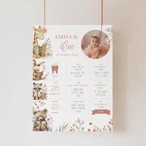 Könnte beinhalten: Personalisiertes Poster zum ersten Geburtstag mit einem Foto eines kleinen Mädchens. Das Poster enthält den Text "Emma ist eins" und Details wie Größe (66 cm), Gewicht (10 kg) und Lieblingsdinge, alles in einem sanften Pastellfarbschema.