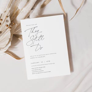 May include: A white invitation card with black script text that reads "They Still Do" for an anniversary party. The card includes details such as the date, time, location, and RSVP information. Dried floral elements are in the background.