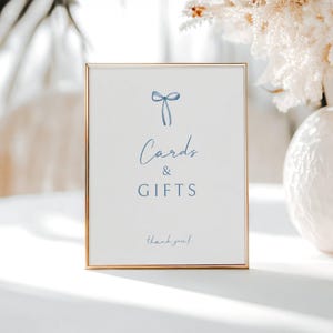 May include: A framed sign with a gold border and a white background. The sign has a blue bow illustration at the top, with the words "Cards & GIFTS" in a script font. The words "thank you!" are at the bottom.