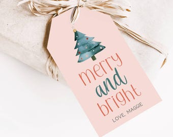 Peut inclure: Étiquette cadeau rose avec une illustration aquarelle d'un sapin de Noël et le texte "merry and bright" en rouge et bleu. L'étiquette comprend également le texte "LOVE, MAGGIE" en rouge.