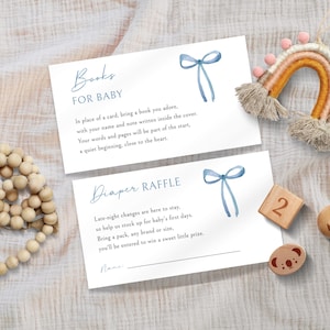 May include: Two white cards with blue watercolor bow illustrations and text for a baby shower. One card reads "Books FOR BABY" and the other reads "Diaper RAFFLE". A wooden rainbow and wooden blocks are also in the image.
