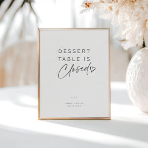May include: A rectangular sign in a gold frame with a white background. The text "DESSERT TABLE IS Closed" is displayed in black, with the word "Closed" in cursive. The sign also includes names and a date.