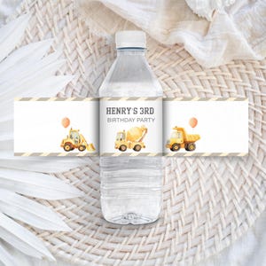 Puede incluir: Una botella de agua transparente con una etiqueta personalizada para una fiesta de 3er cumpleaños. La etiqueta presenta ilustraciones de vehículos de construcción, incluyendo una excavadora, una hormigonera y un camión volquete, con un globo. El texto en la etiqueta dice "HENRY'S 3RD BIRTHDAY PARTY."