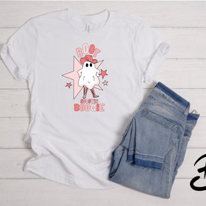 May include: White t-shirt with a pink and red graphic of a ghost wearing a cowboy hat and boots. The text "BOOT SCOOTIN' BOOGIE" is below the ghost.