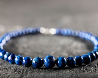 May include: A necklace made of dark blue lapis lazuli beads. The beads are round and smooth, and the necklace is strung on a silver chain.