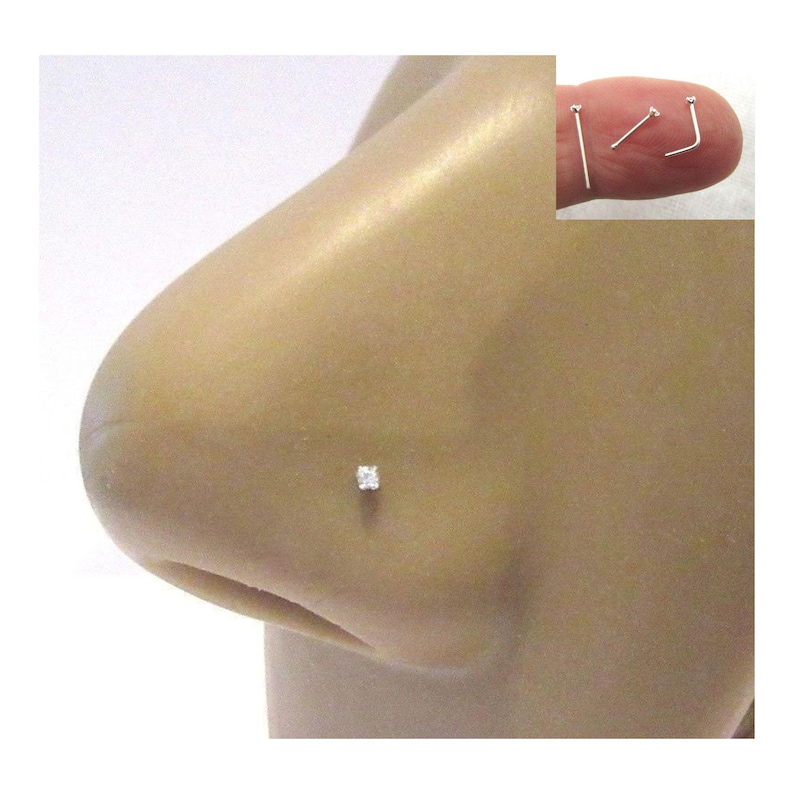 May include: A close-up of a person's nose with a small, clear, square-shaped nose ring stud.