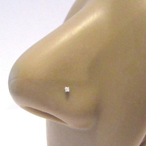 May include: A close-up of a clear nose ring with a small, clear gemstone. The ring is on a model's nose.