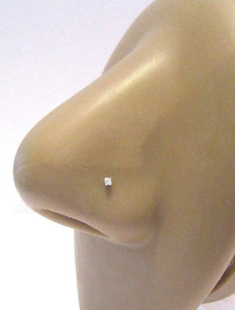May include: A close-up of a clear nose ring with a small, clear gemstone. The ring is on a model's nose.