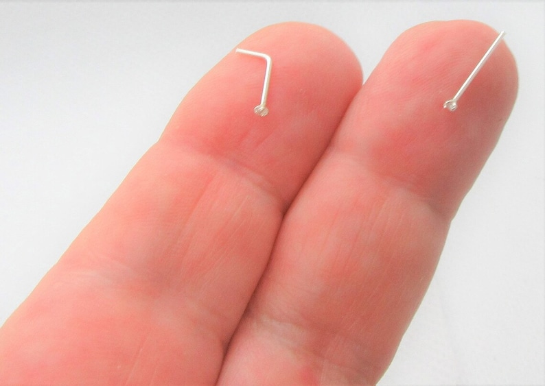 May include: Two silver nose rings with small clear stones on the ends. The rings are shown on a finger.