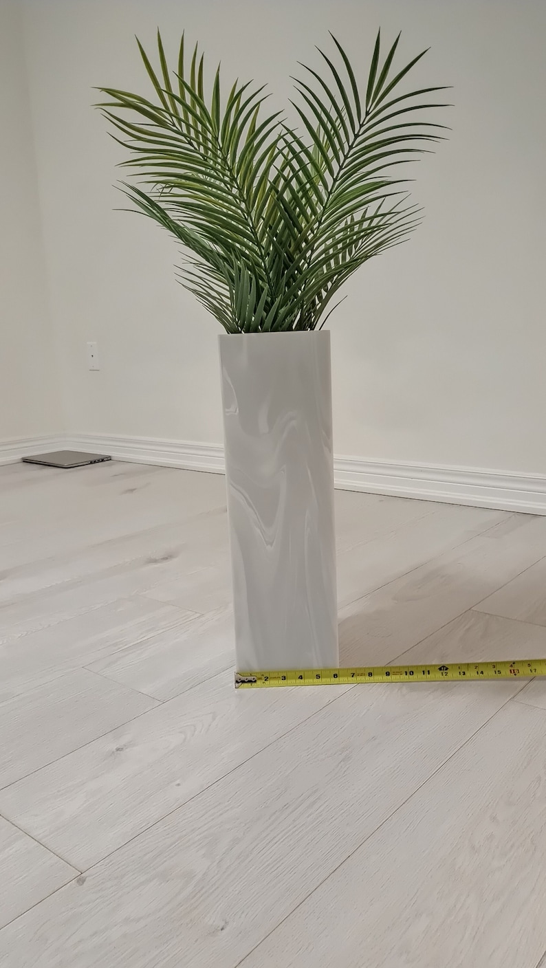 以下が含まれることがあります： 白い渦巻き模様のセラミックの花瓶に、緑の人工ヤシの木が挿されています。花瓶の高さは43cmで、白い木製の床の上に置かれています。