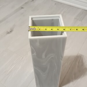 以下が含まれることがあります： グレーの大理石模様の白いセラミックの花瓶。花瓶は高さ23cmで正方形です。