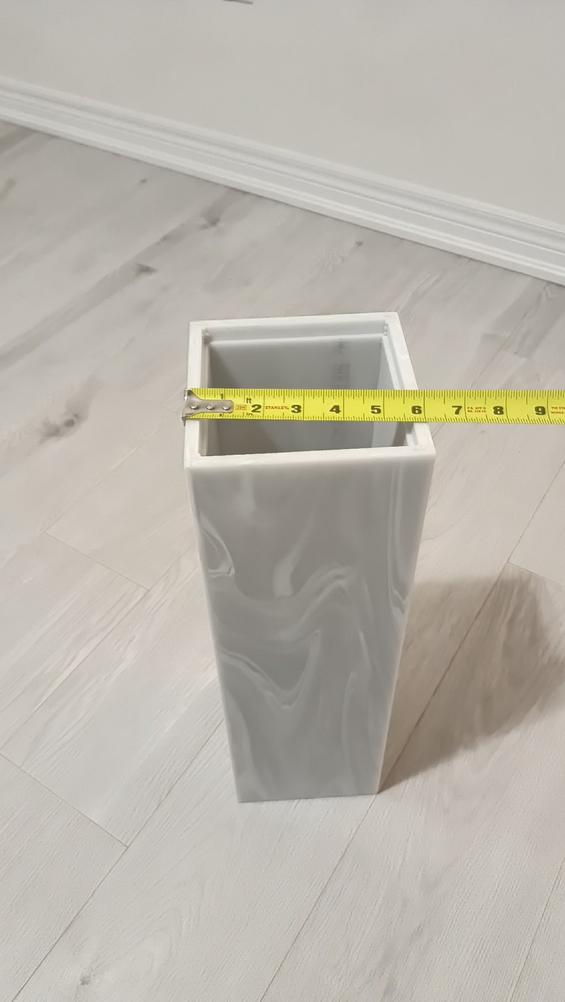 以下が含まれることがあります： グレーの大理石模様の白いセラミックの花瓶。花瓶は高さ23cmで正方形です。