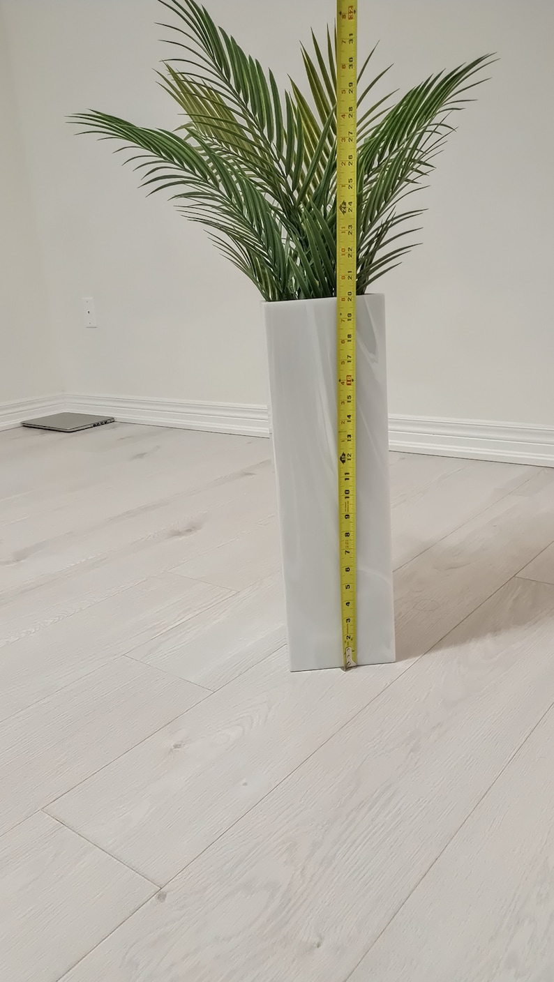 以下が含まれることがあります： 白いセラミックの花瓶にヤシの木が入っています。花瓶の高さは35.5cmで、黄色のメジャーで測定されています。