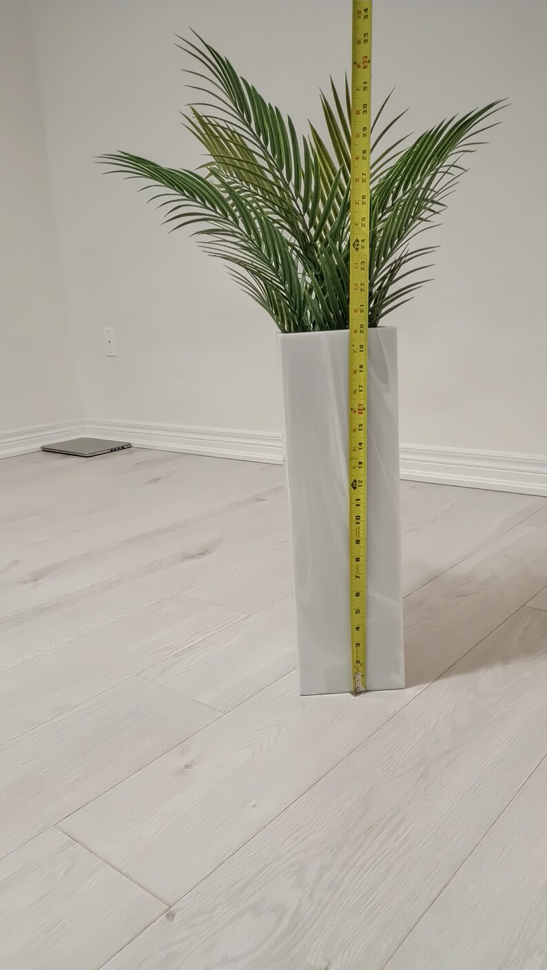 以下が含まれることがあります： テクスチャ加工された表面を持つ白いセラミックの花瓶で、高さ71cm、緑の人工ヤシの木が入っています。