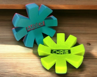 May include: Two 3D printed star-shaped ornaments with the names "Amber" and "Chris" cut out. The top ornament is teal with pink accents and the bottom ornament is bright yellow.