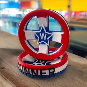 May include: A red, white, and blue circular object with a white star in the center and the letter "W" inside the star. The object is labeled "RUNNER" in black letters on a white and red stripe.