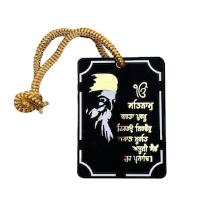 May include: Black and gold decorative tag with a gold rope. The tag features a white image of a man with a beard and turban. The text on the tag reads "ੴ ਸਤਿਗੁਰ ਪ੍ਰਸਾਦਿ" in gold lettering.