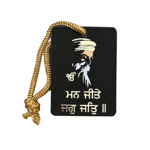 May include: A black rectangular tag with a gold rope attached. The tag features a white and gold illustration of a man with a beard and turban. The text "ਮਨ ਸੀਤ" and "ਨਗਾ ਸੀਤ" is written in gold on the tag.