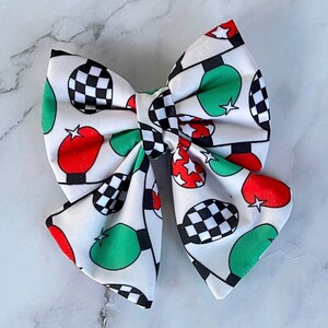 May include: A white bow with a checkered, red, and green pattern. The bow is made of fabric and has a ruffled texture.