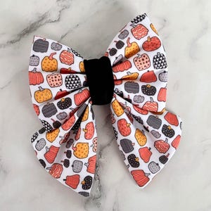 May include: A white bow tie with a black velvet centre, featuring a pattern of orange and black pumpkins.