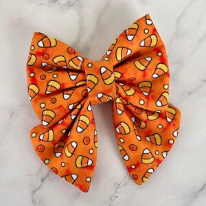 Könnte beinhalten: Orangefarbener und weißer Bogen mit einem Mais-Muster. Der Bogen ist aus Stoff und hat einen Bindeverschluss.