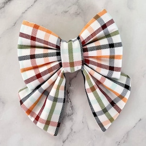 May include: A large plaid bow with a white background and orange, red, green, and black plaid pattern.